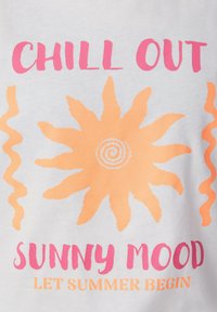 T-shirt en coton blanc avec un texte imprimé rose et orange. Présente un design de soleil avec des accents ondulés et un texte disant "DÉTENDS-TOI" et "HUMEUR ENSOLEILLÉE".