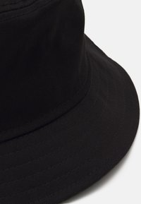 Gorra de cubo negra hecha de algodón, con un ala ancha y plana y costuras verticales para textura. Diseño simple y funcional.
