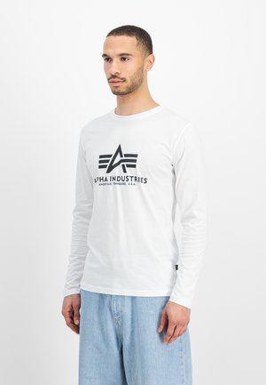 Langärmliges weißes T-Shirt mit einem schwarzen Logo, auf dem "Alpha Industries" steht, und einem geometrischen Akzentdesign auf der Vorderseite.