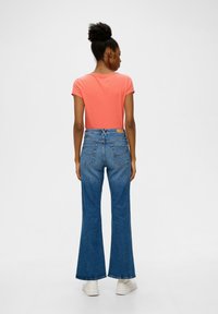 Korte mouwen koraalkleurig T-shirt, gecombineerd met hoge taille spijkerbroek met flared pijpen, dat de textuur van denim en een subtiel ontwerp van een achterzak toont.