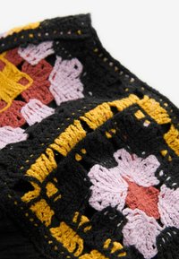 Tissu en crochet multicolore présentant des motifs floraux en rose, jaune, noir et marron, avec des points texturés et des sections ajourées.