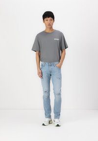 Grå kortermet t-skjorte med logo, lyseblå revne jeans og hvite joggesko med grønne detaljer. Slim fit med rett ben-design.