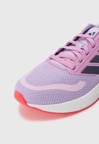 Chaussure de sport violette avec tissu en maille, partie supérieure texturée, lacets et accents roses. Dotée d'une semelle blanche avec un dessous rouge et d'une étiquette "CLOUDFOAM".