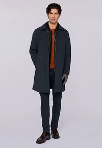 Tmavě modrý kabát s knoflíkovou přední částí, nošený přes černou koženou bundu a oranžovou košili. Elegantní střih, doplněný námořnickými kalhotami a hnědými botami.