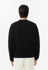 Sudadera negra de corte relajado, con mangas largas y cuello redondo. Textura suave con puños y dobladillo acanalados.