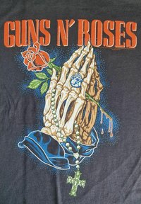 Zwarte t-shirt met een grafische afbeelding van skelet handen in gebed, een rode roos, groene rozenkrans en "GUNS N' ROSES" in vet oranje tekst.