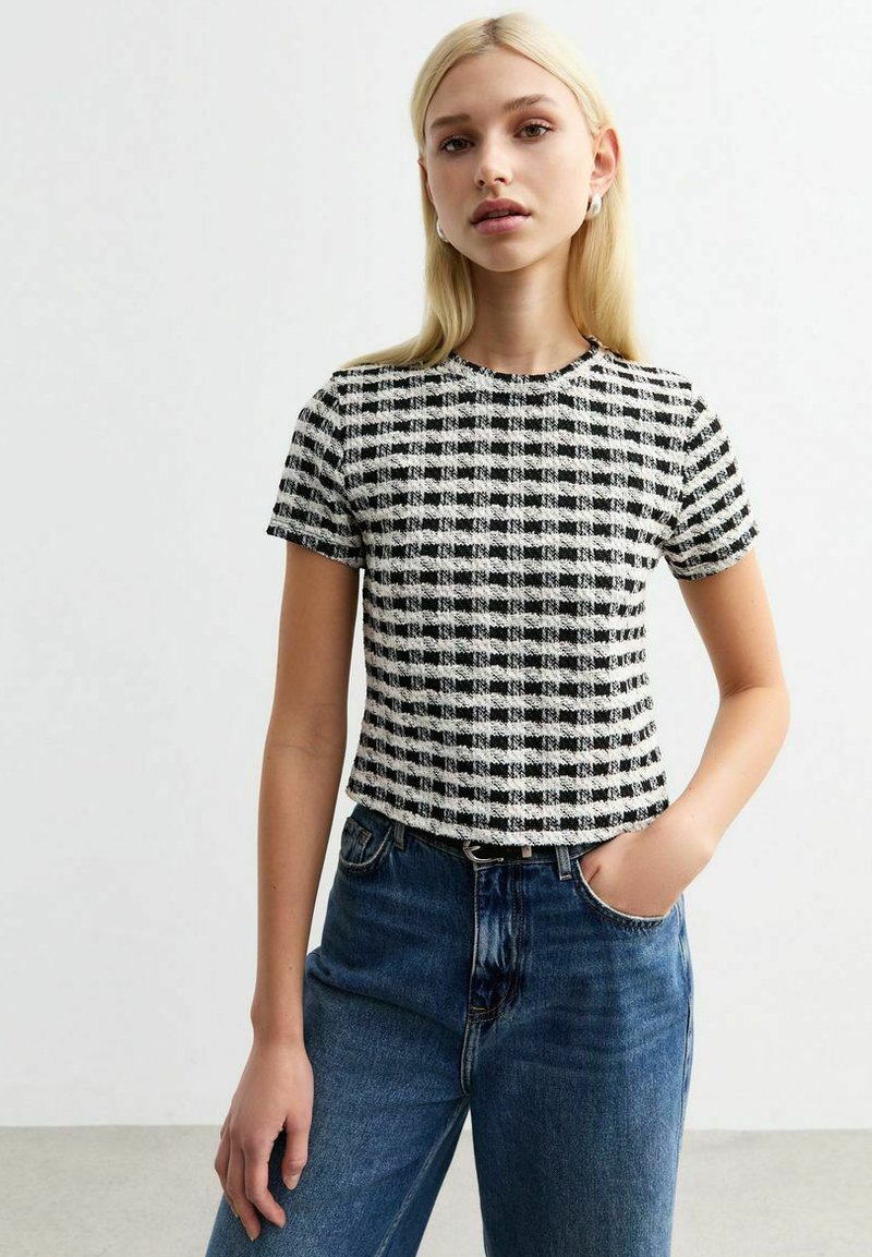 Kortärmad topp i svart och vit rutigt mönster, texturerad tyg, rund hals, croppad passform. Sammanfogas med högmidjade blå jeans.