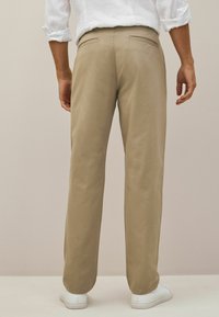 Beige bomullbyxor sedd bakifrån, med två bakfickor, rak passform och vita sneakers som kompletterar outfiten.