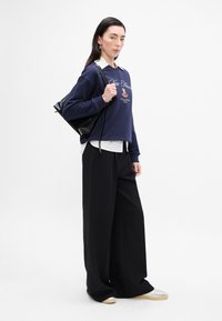 Granatowy sweter z napisem i kwiatowym wzorem, założony na białą koszulę; szerokie czarne spodnie; czarna torebka; sneakersy z przezroczystą podeszwą.