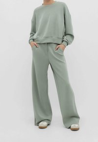 Sudadera verde claro con hombros caídos y pantalones de pierna ancha a juego, ambos hechos de una tela suave y lisa. Zapatillas blancas como calzado.