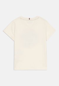 Κρεμ κοντομάνικο μπλουζάκι με μια μικρή μαύρη, λευκή και κόκκινη ρίγα στη πλάτη του γιακά, ακίνητο σε άσπρο φόντο.