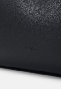 Surface en cuir texturé noir avec le nom de la marque "PATRIZIA PEPE" en relief et le logo, centrés près du bas.