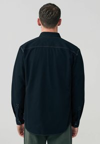 Long-sleeve shirt, dark navy color, textured fabric, straight cut, visible stitching, button cuffs, back yoke design, casual style.