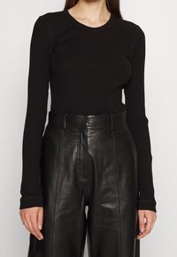 Maglietta nera a maniche lunghe con coste abbinata a pantaloni in pelle nera a vita alta, caratterizzati da una texture liscia e una vestibilità tailored.