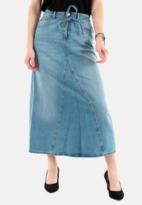Lichtblauwe denim maxi rok met een hoge taille, strikdetail, voornaad en rafelige onderrand. Gecombineerd met zwarte hoge hakken.