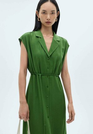 Rochie verde cu mâneci scurte, cu închidere cu nasturi pe față, talie legată și textură fină. Modelul ține o geantă de culoare deschisă.