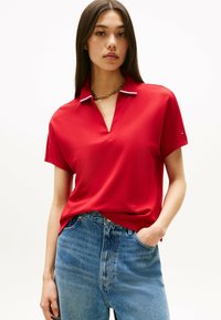 Maglietta polo rossa con scollo a V, maniche corte e colletto a righe a contrasto. Abbinata a jeans in denim blu a vita alta.