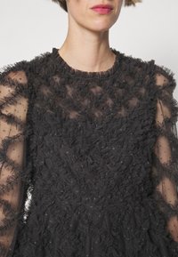 Femme portant une robe noire transparente avec des couches de tulle froncé et de petits motifs étoilés sur les manches.