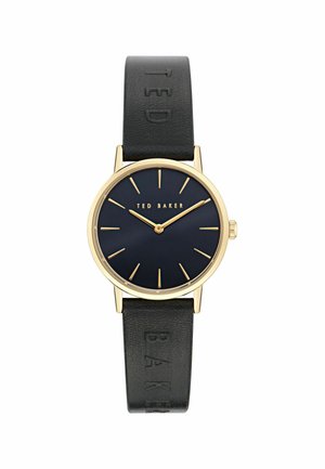 Rund klocka med guldtonad boett, marinblå urtavla, guld timmarkörer och svart läderrem prydd med "TED BAKER."