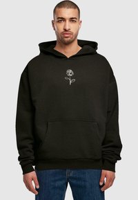 Sort hættetrøje i blødt stof med en stor lomme foran, prydet med en hvid rosebroderi på brystet. Casual pasform med snøre ihætten.