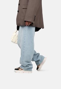 Blazer gris surdimensionné, jeans baggy bleu clair et baskets noires et dorées à motifs. Les accessoires incluent un sac à main texturé blanc.