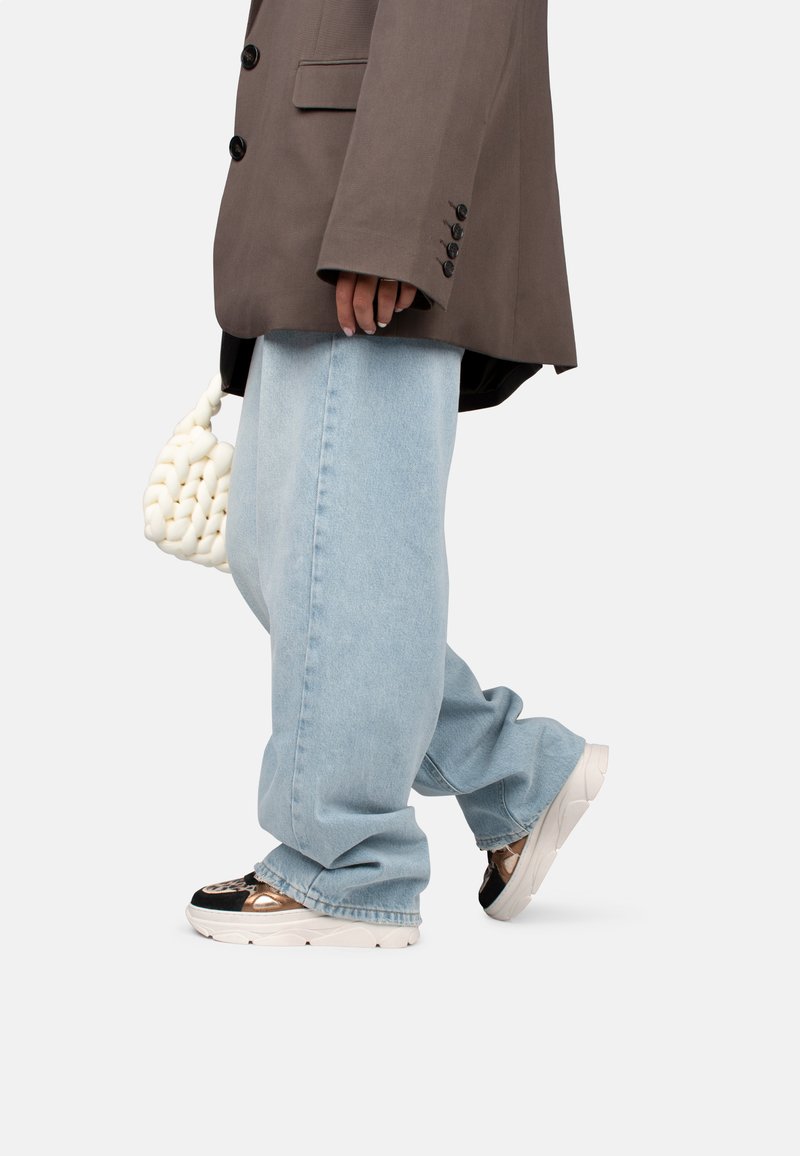 Blazer gris surdimensionné, jeans baggy bleu clair et baskets noires et dorées à motifs. Les accessoires incluent un sac à main texturé blanc.