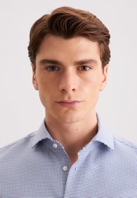 Blauw en wit gestreept shirt met een knoopsluiting op de kraag. De stof is geweven en heeft een klein geometrisch patroon en een gestructureerde afwerking.