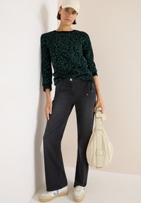 Maglione verde scuro con motivo leopardato, abbinato a jeans flare neri e scarpe da ginnastica bianche con accenti blu. Borsa di colore chiaro.