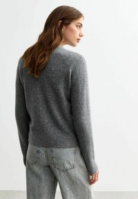 Maglione grigio lavorato a maglia, scollatura rotonda, maniche lunghe, stile aderente. Indossato con jeans chiari a vita alta, texture morbida, design casual.