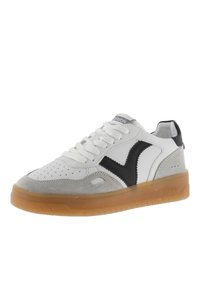 Sneaker bianco e grigio con accenti neri, punta perforata, suola in gomma spessa e lacci. Presenta un design curvo e materiali a contrasto.