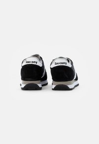 Zwarte suède sportieve schoenen met een grijs en wit ontwerp. De achterkant toont het "Saucony" logo en een gestructureerde rubberen zool.