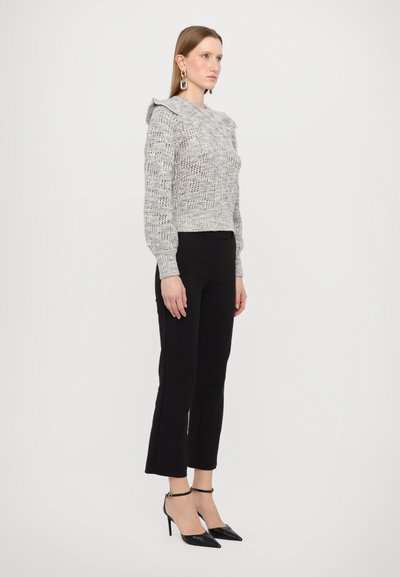 Pull en maille grise avec un tissage texturé et ouvert, agrémenté d'un col festonné, associé à un pantalon cropped noir et des escarpins noirs à bout pointu.