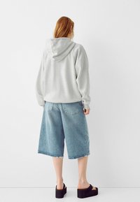 Felpa grigia con una vestibilità comoda e cappuccio, abbinata a culotte in denim blu chiaro con orlo sfrangiato, indossate con sandali platform neri.