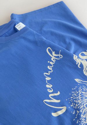 Blue sweatshirt folded with white cursive text reading "Mermaids" and partial sea-themed illustration on front.