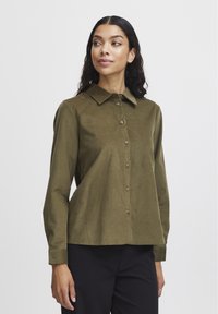Camicetta verde oliva scuro con colletti, maniche lunghe e una vestibilità leggermente ampia, realizzata in un tessuto testurizzato.