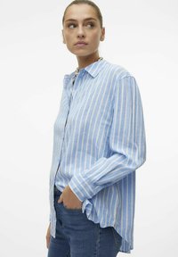 Light blue striped shirt in a soft fabric, featuring a button-down front, long sleeves, and a relaxed fit. Paired with fitted jeans.