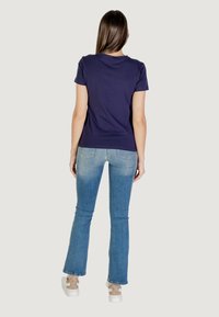 T-shirt navy a maniche corte, abbinato a jeans a zampa d'elefante di colore blu chiaro e sneakers con un accento a fantasia. Vista posteriore, design semplice.