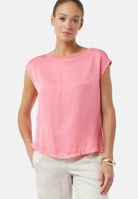 Roze T-shirt met korte mouwen en een ronde hals. Zacht materiaal, ontspannen pasvorm, gladde textuur en een onafgewerkte zoom. Draagt met lichtgekleurde broeken.