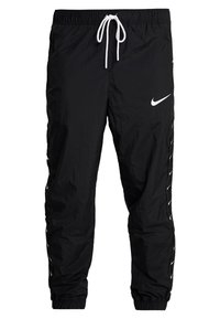 Černé nylonové tepláky s elastickým pasem, bílým šňůrkem a logem Nike. Obsahují boční pruhy s malými logy podél nohou.