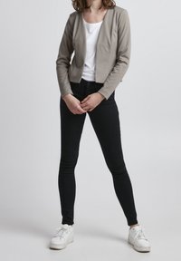 Ljusgrå, figursydd jacka i kombination med en vit skjorta, svarta skinny jeans och vita sneakers. Slät tyg med en enkel design.