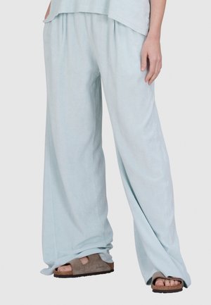 Lichtblauwe wijde broek van een zachte stof met een relaxte pasvorm, voorzien van een comfortabele tailleband en gedragen met bruine instapsandalen.