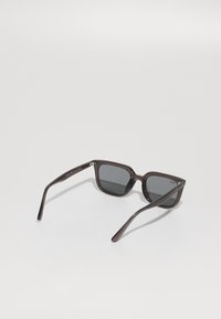 Ochelari de soare dreptunghiulari cu lentile gri închis și cadru din plastic transparent de culoare maro închis. Brațele subțiri au detalii subtile de branding.