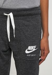 Černé pletené tepláky mají stahovací pas, boční kapsy a bílé logo Nike s textem "JUST DO IT" na levém stehně.