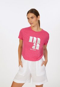 Pink short-sleeve t-shirt with a textured finish, featuring bold white graphic lettering. Paired with white linen shorts.