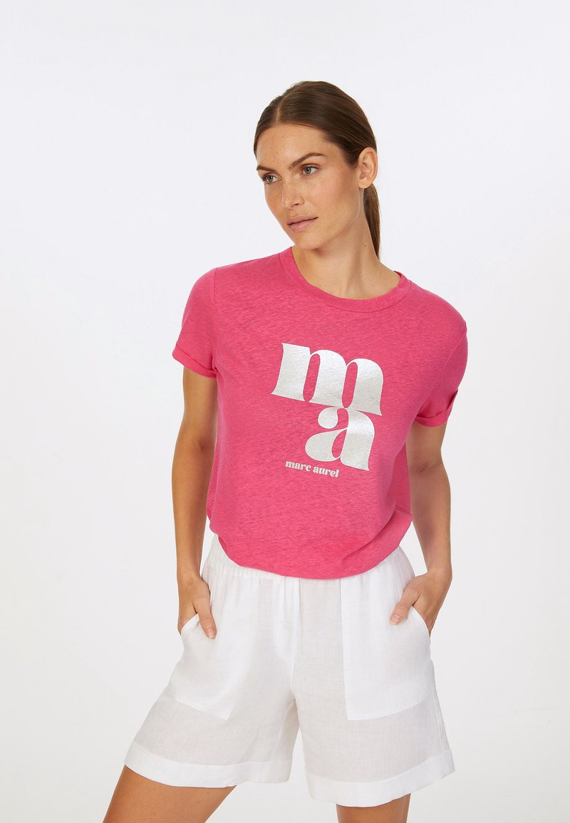 Pink short-sleeve t-shirt with a textured finish, featuring bold white graphic lettering. Paired with white linen shorts.