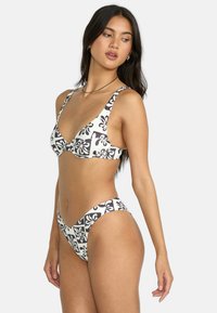 Completo bikini bianco e nero con top triangolare e slip a vita alta. Tessuto liscio con spalline larghe e motivi floreali.