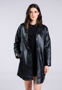 Svart läderrock med avslappnad passform, stor krage, knapplist och sidofickor. Slät textur och knälång design.