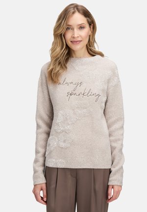 Jasno beżowy sweter z miękkiej tkaniny, z błyszczącymi włóknami i haftowanym wzorem "zawsze błyszczący" z przodu.