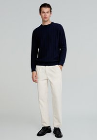 Navy niebieski sweter prążkowany z długimi rękawami, w połączeniu z białymi spodniami w luźnym fasonie i czarnymi sznurowanymi butami. Prosty, nowoczesny design.