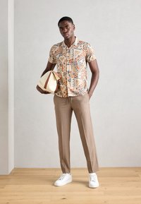 Kortærmet mønstret skjorte i beige med geometriske former, parret med lysebrune skræddersyede bukser og hvide sneakers.